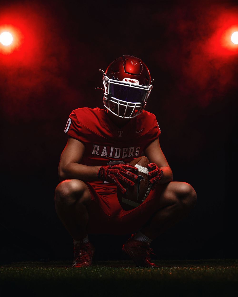 Football player in red Raiders uniform strikes dramatic pose under red lighting in dark setting.