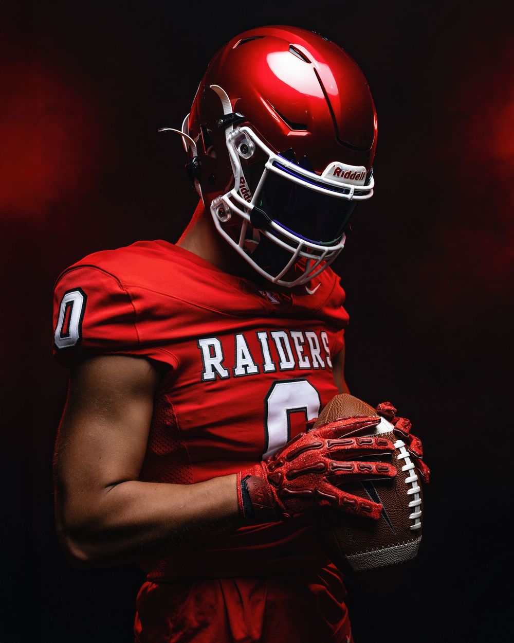 Close-up view of red football glove gripping a football against a dark background with dramatic lighting.