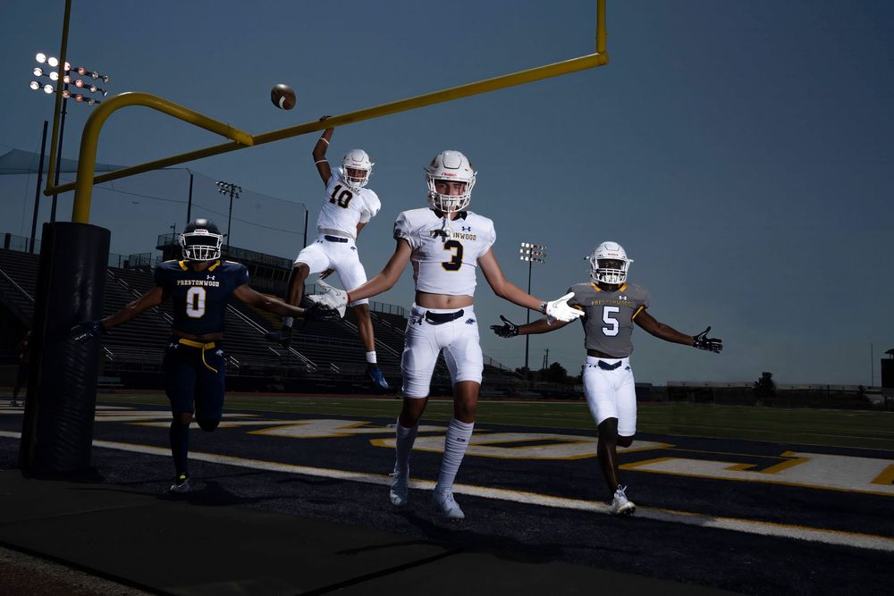 Football players celebrate in a dynamic pose under a field goal post during a sunny day photoshoot.