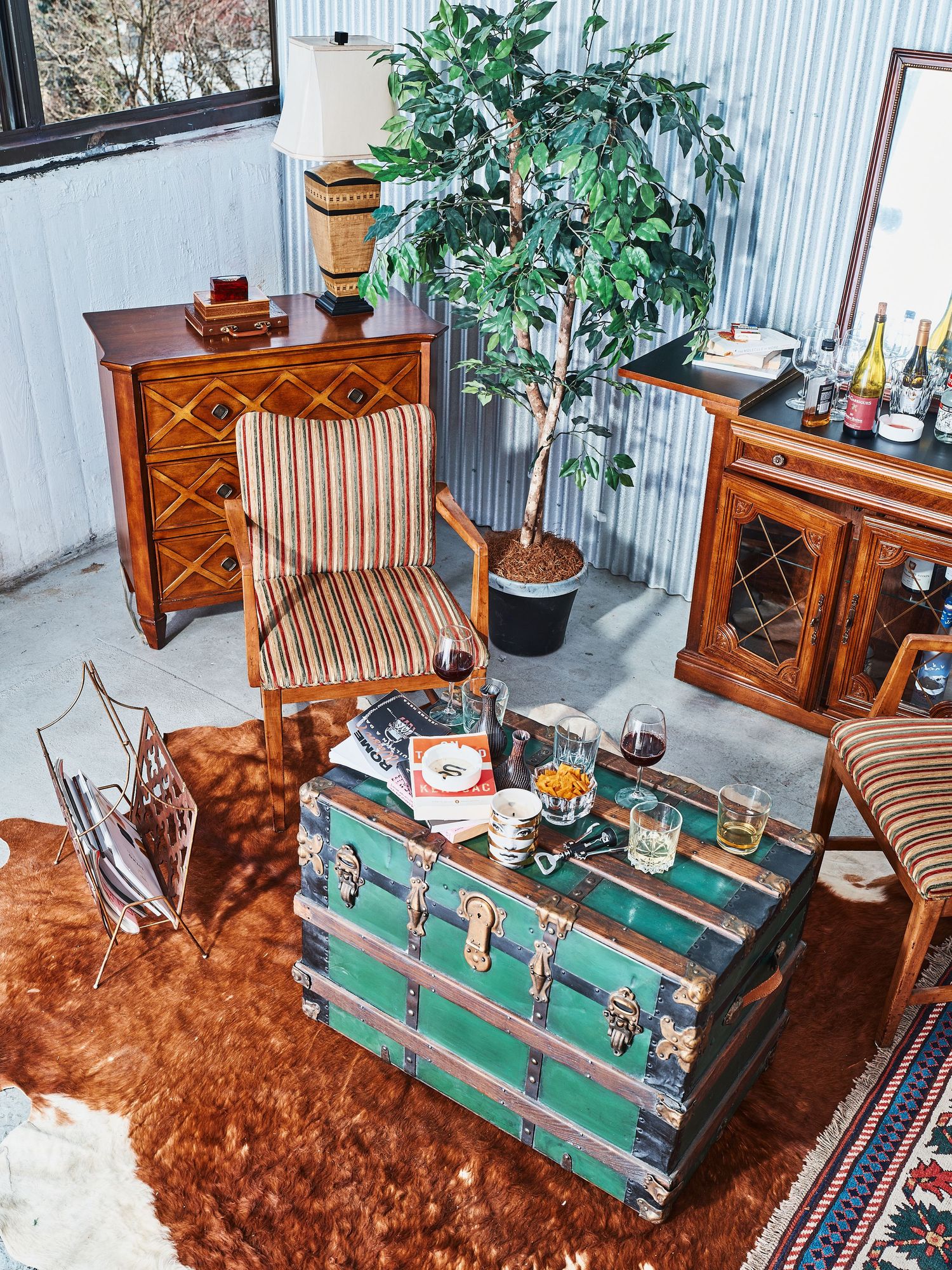 Cozy living room corner with antique green trunk, striped chairs, and artificial plant.
