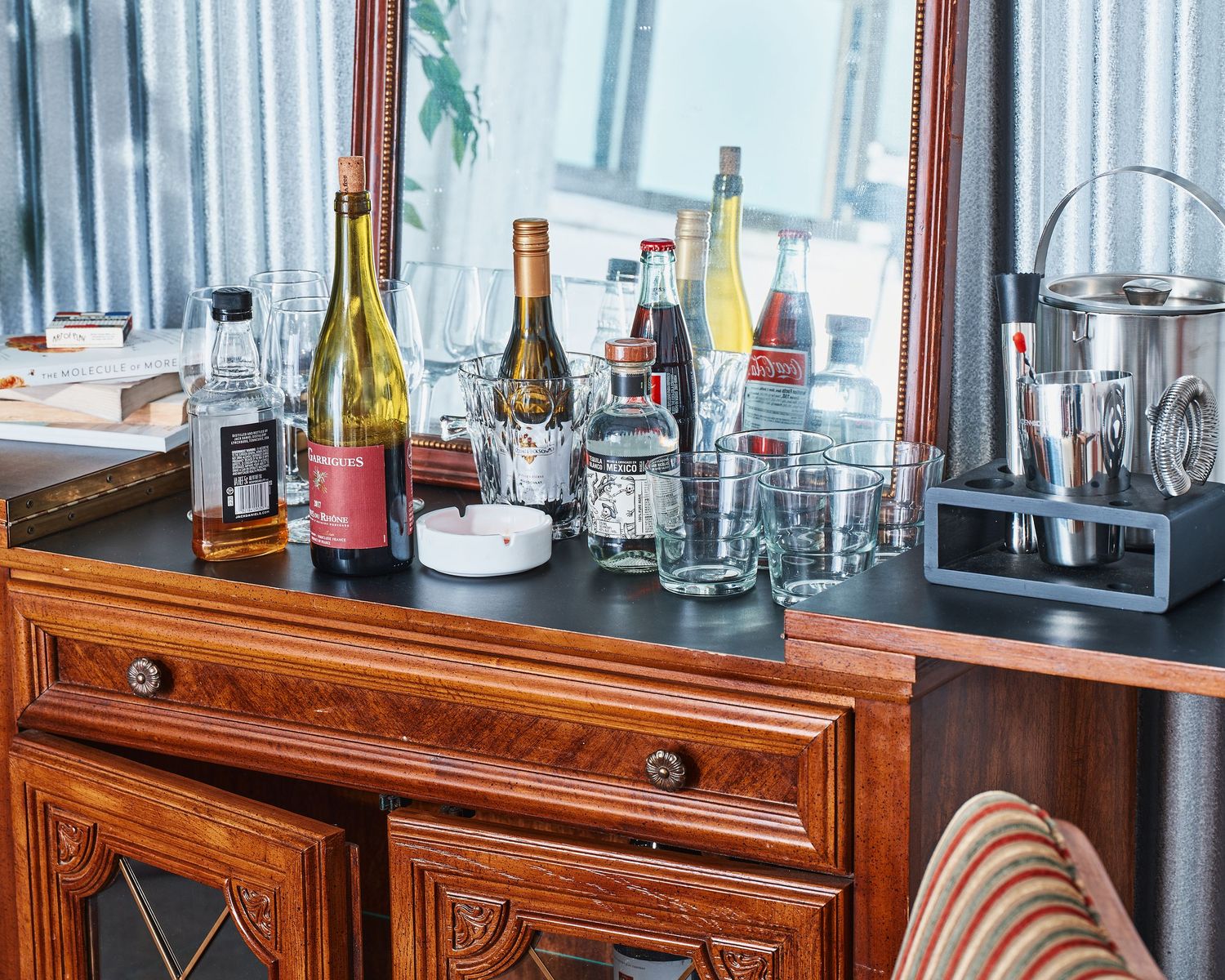 Wooden sideboard with collection of wine bottles and glassware arranged on top.