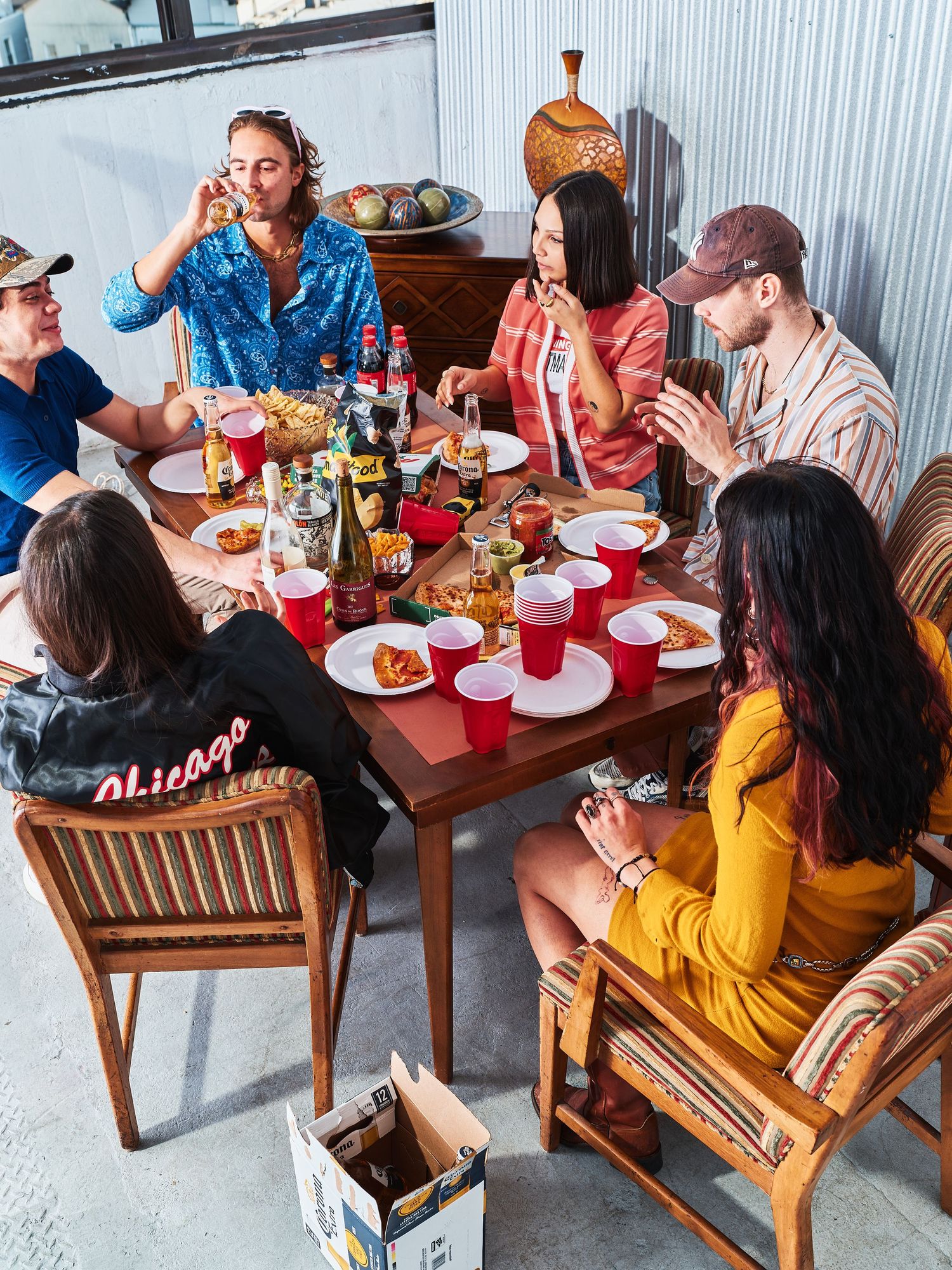 Group gathered around wooden table enjoying casual meal with snacks and drinks.