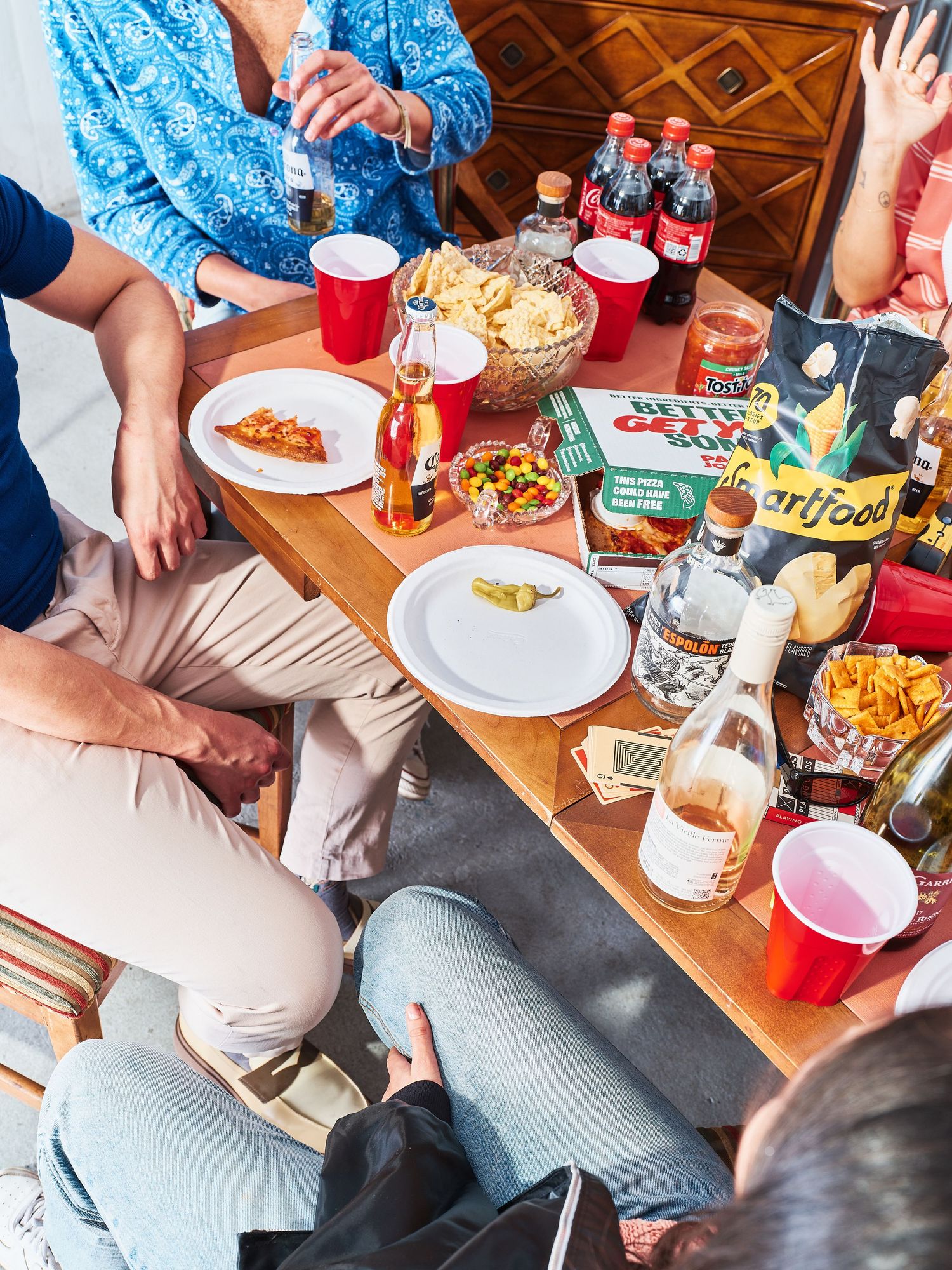 Overhead view of casual dining spread with pizza slices, chips and drinks on wooden table.