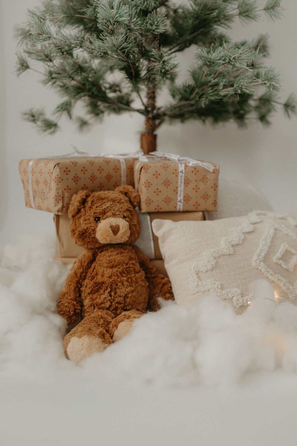 Plush teddy bear and wrapped presents arranged under Christmas tree.