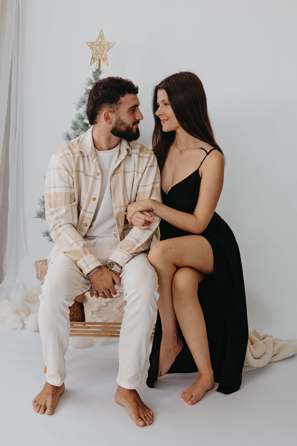 A couple in contrasting black and cream outfits share a romantic moment in front of a Christmas tree.