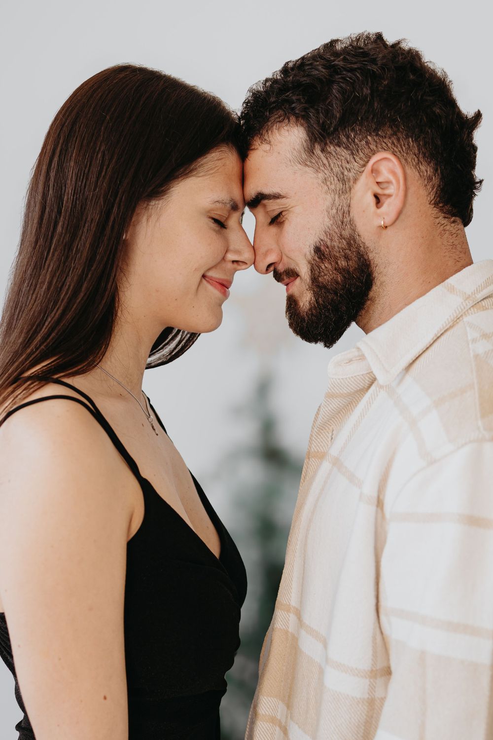 A tender moment captured as a couple touches foreheads against a light background.