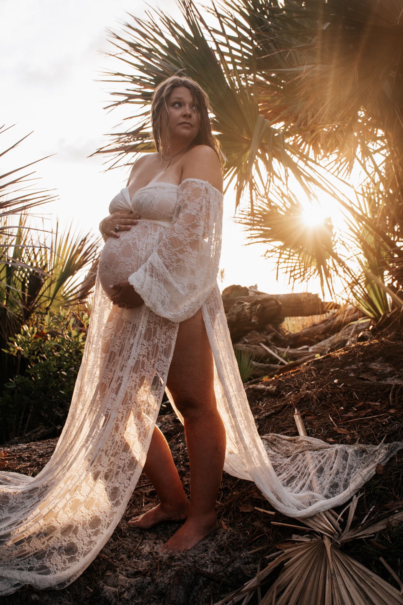 Ethereal maternity photoshoot at sunset with flowing lace dress and palm trees.