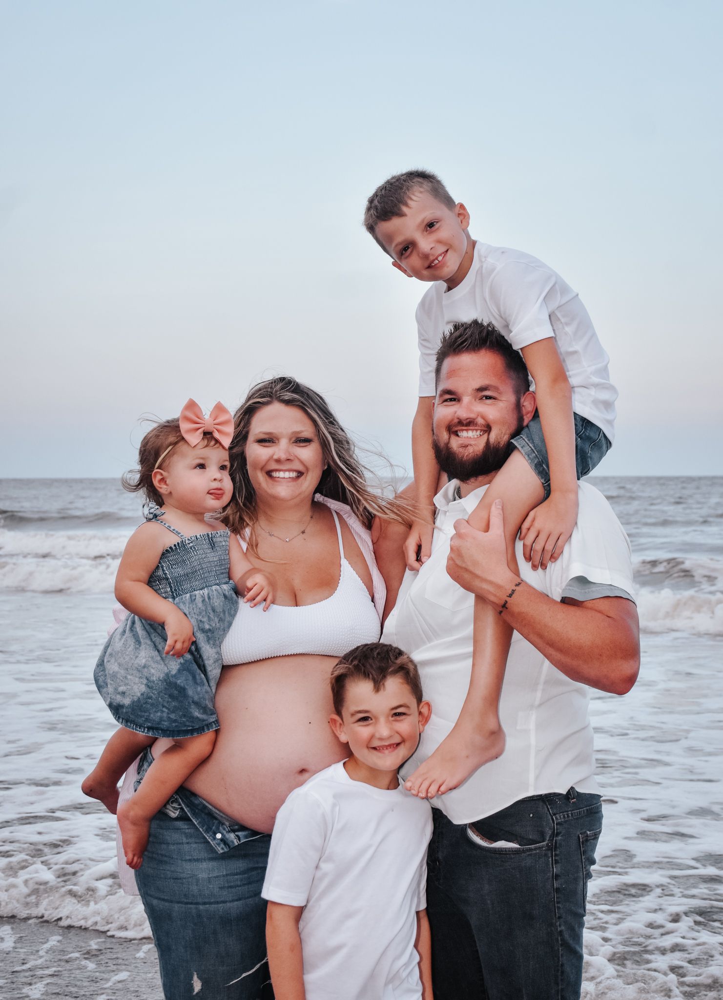 Happy family with expecting mother posing together on beach at dusk.