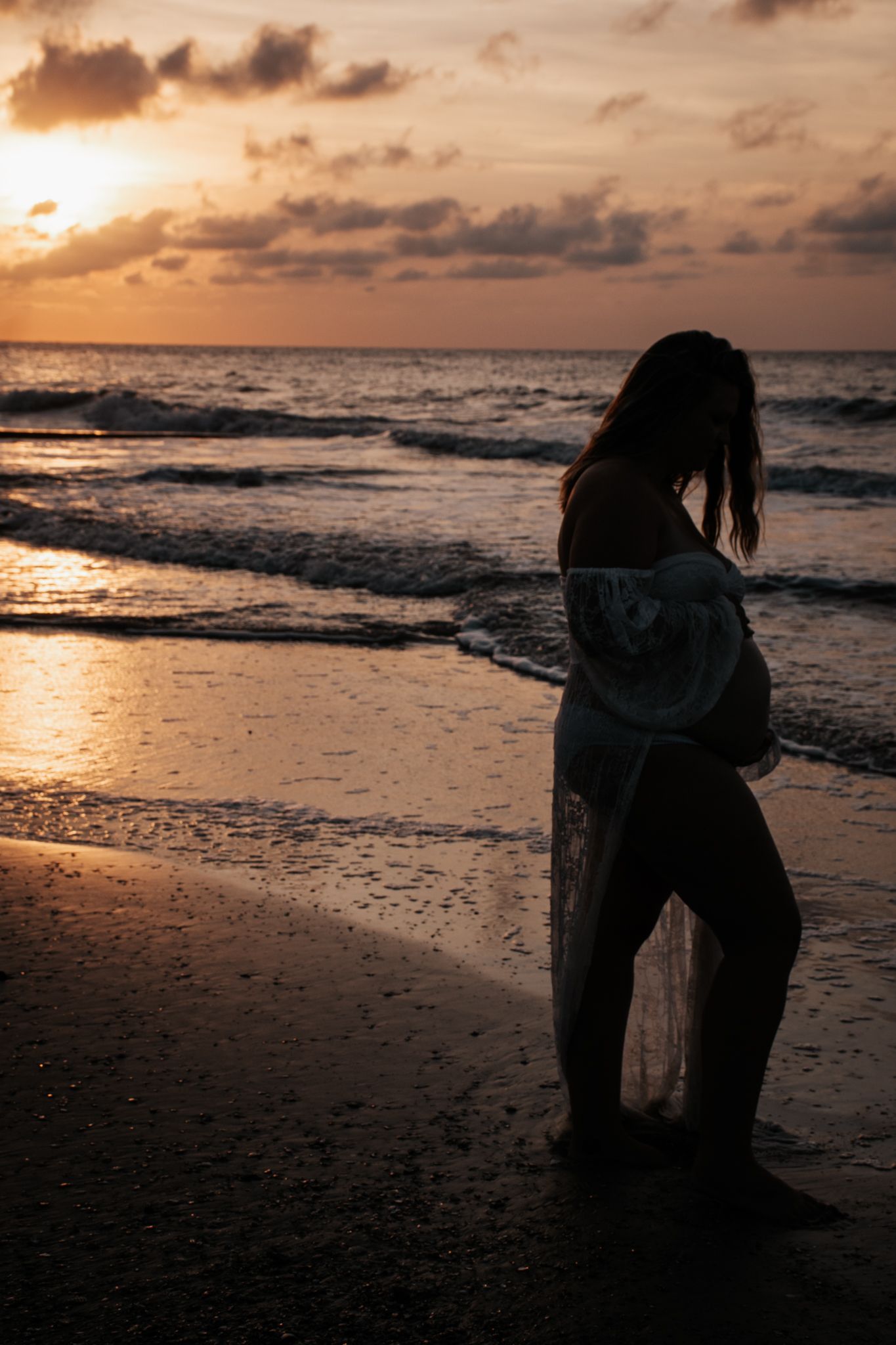 Silhouette of figure in flowing dress on beach at golden sunset.