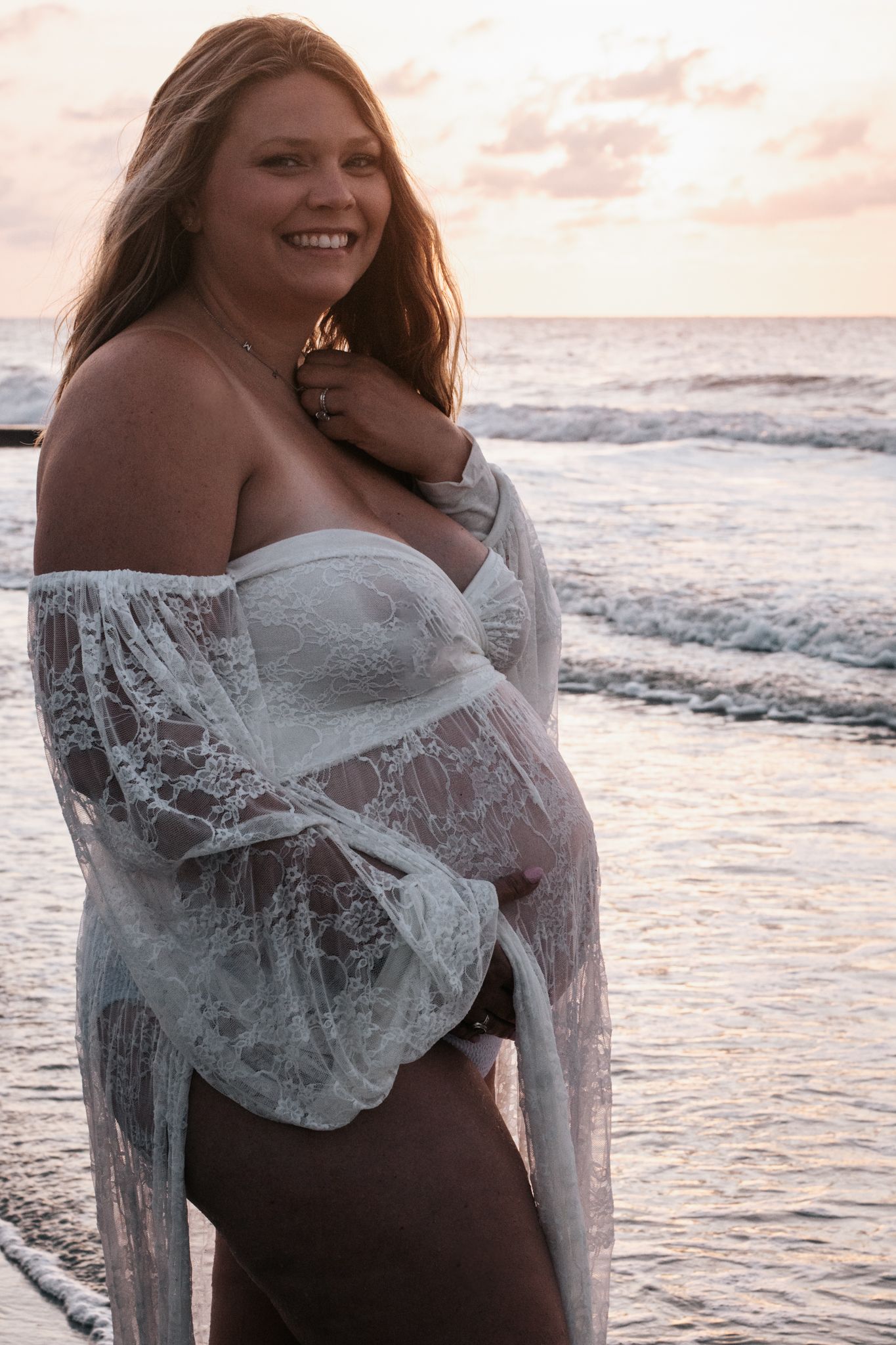 Beach maternity portrait with lace dress at sunset by ocean waves.