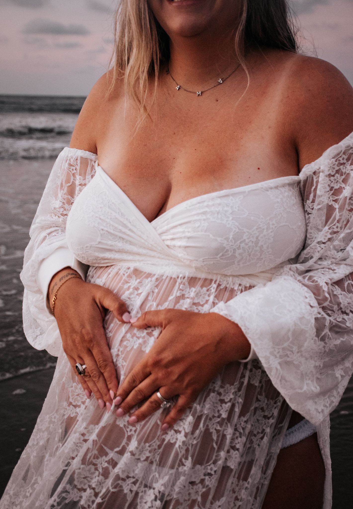 Close-up of white lace maternity dress details against beach backdrop.