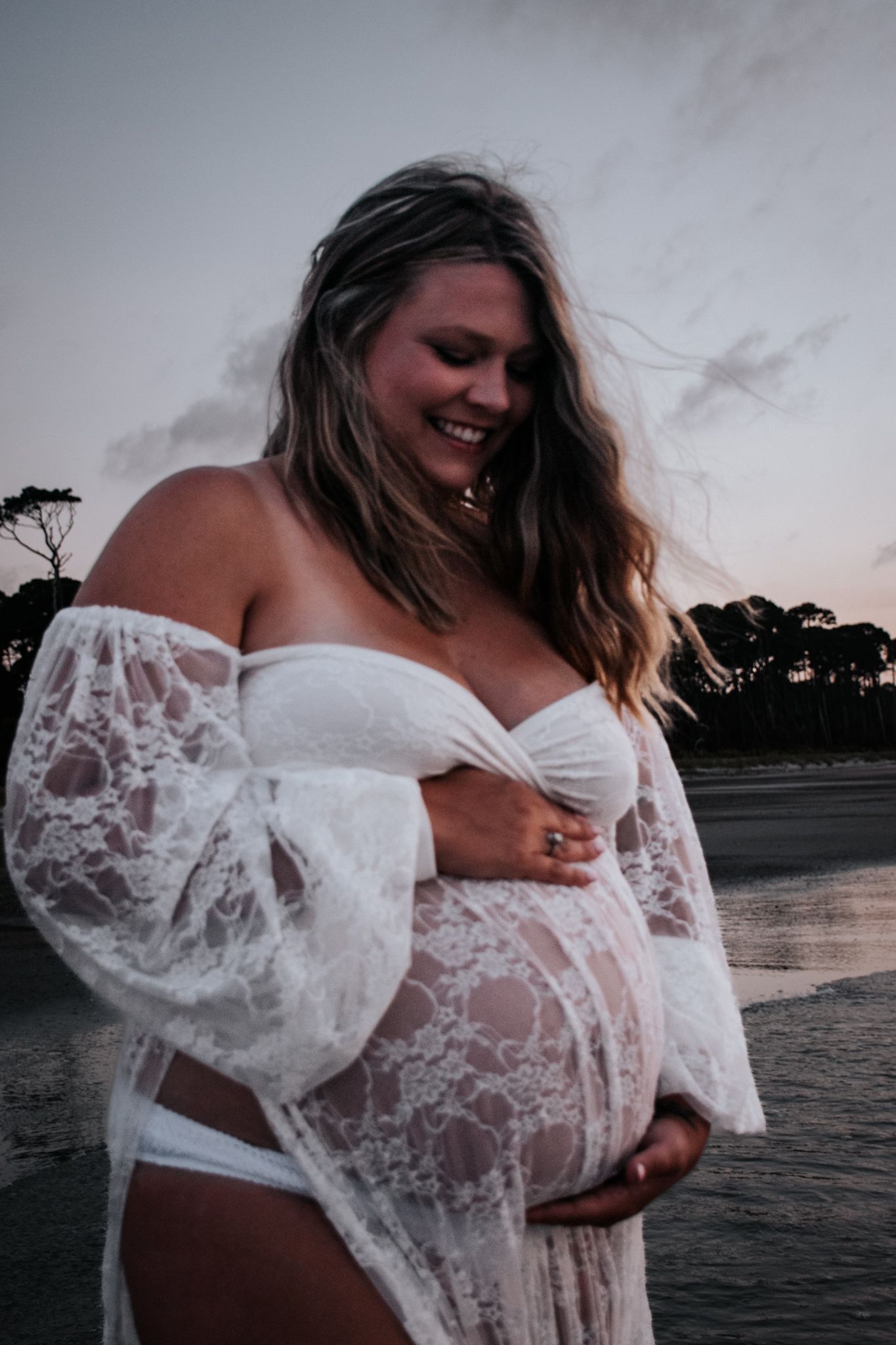 Beach maternity portrait in white lace dress at sunset.