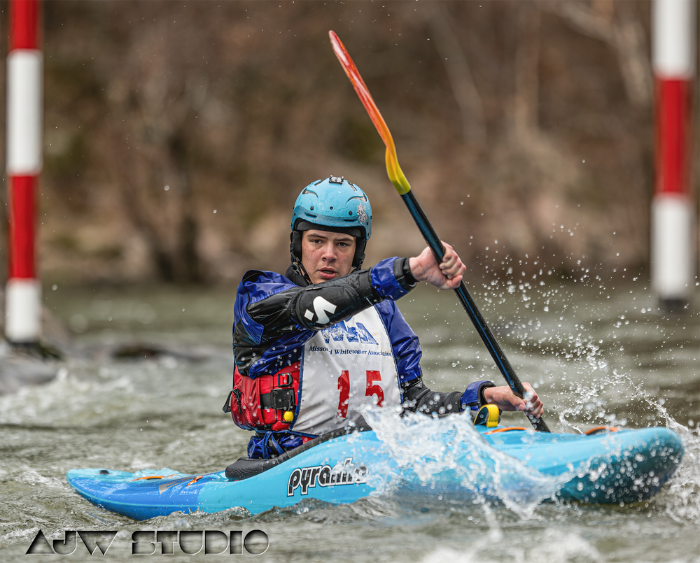 Kayaker in blue helmet and jersey navigates whitewater rapids with a colorful paddle while competing in a race.