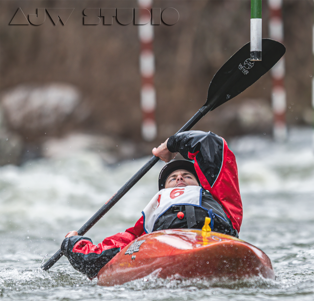 Whitewater kayaker maneuvers through rapids in a red kayak during competition.