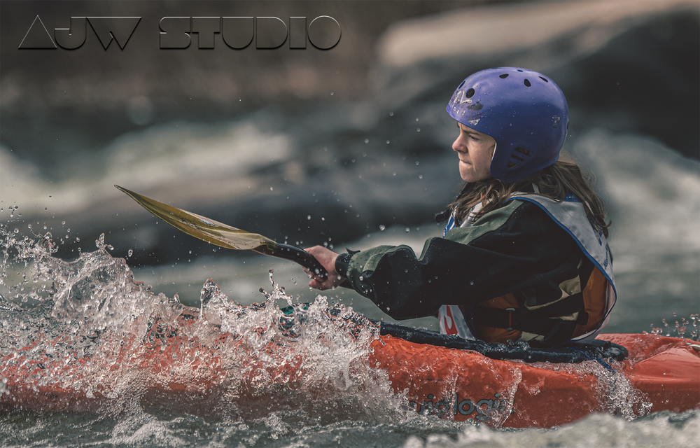 Kayaker in black gear navigates through splashing whitewater rapids in a red kayak.