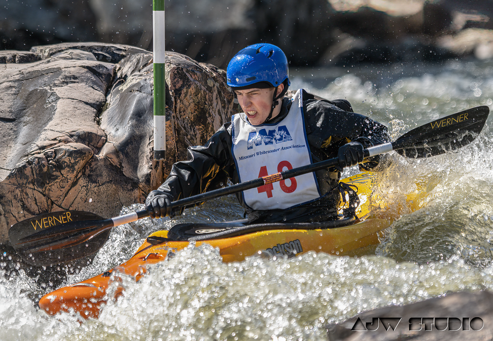 Competitor in blue helmet navigates yellow kayak through rocky whitewater course.