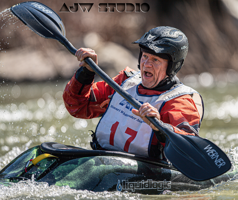 Kayaker in orange life vest and black helmet paddling through whitewater rapids with determination.