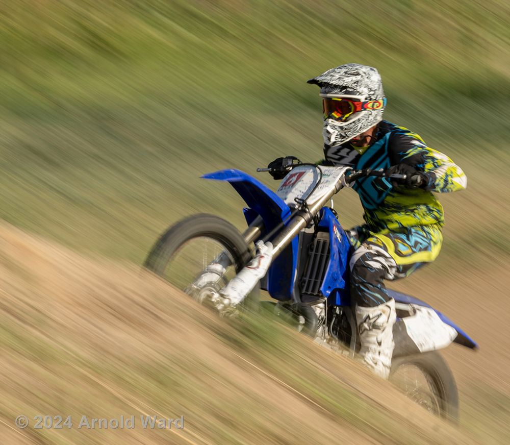 Dirt bike rider speeds along trail with motion blur effect.