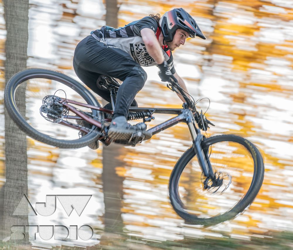 Mountain biker performing aerial jump with autumn foliage background.