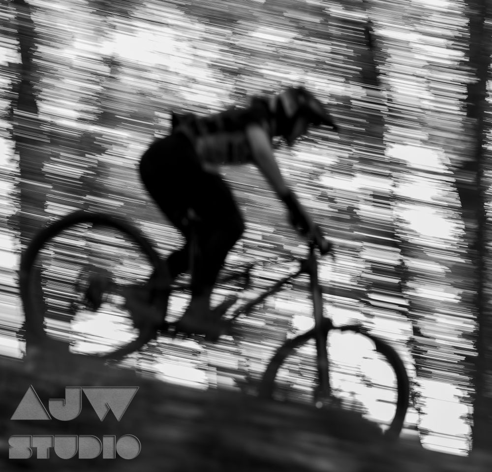 Black and white motion blur of mountain biker performing jump through trees.