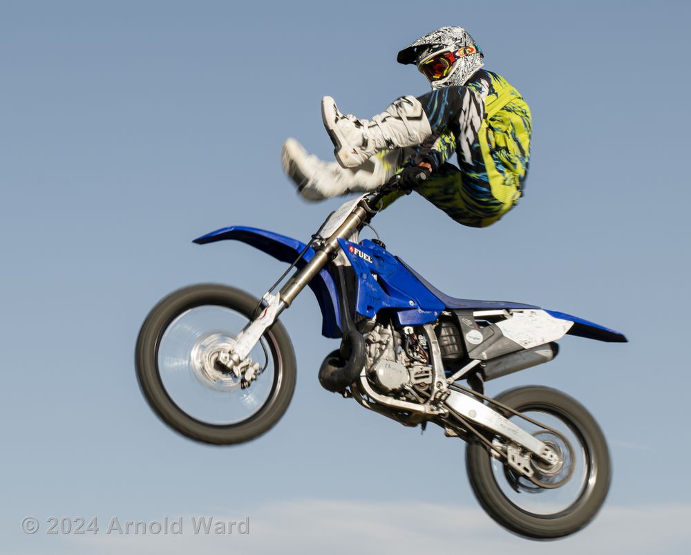 Motocross rider performs aerial stunt with bike against blue sky.