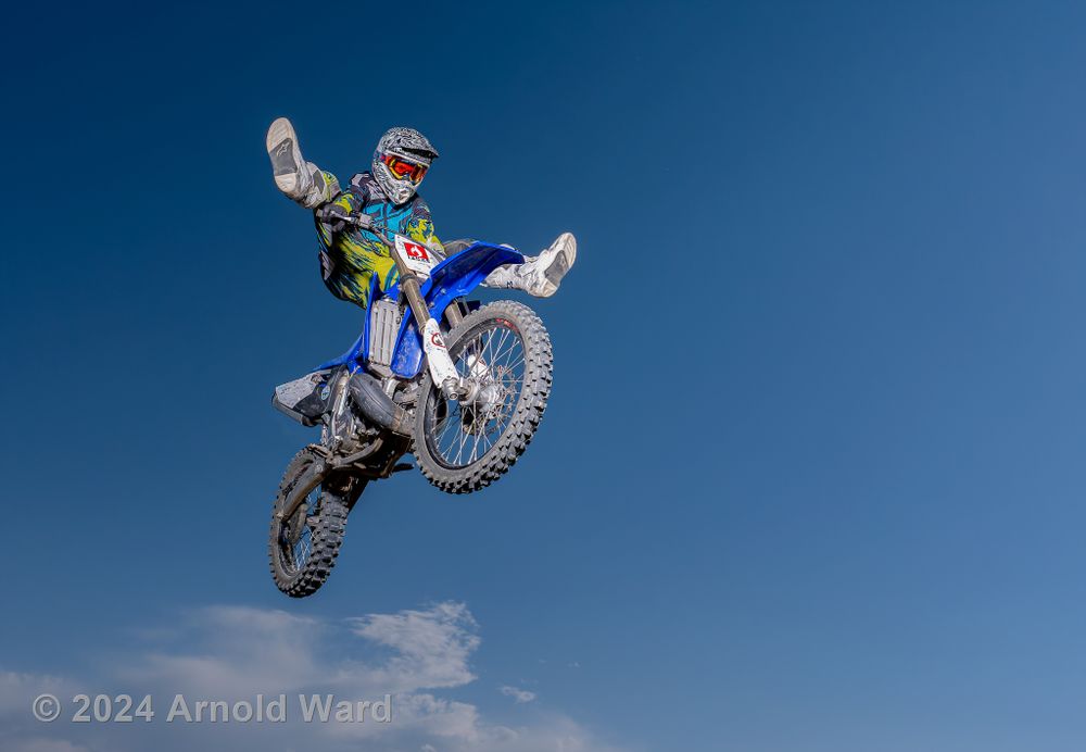 Dirt bike rider performs dramatic aerial stunt against blue sky backdrop.