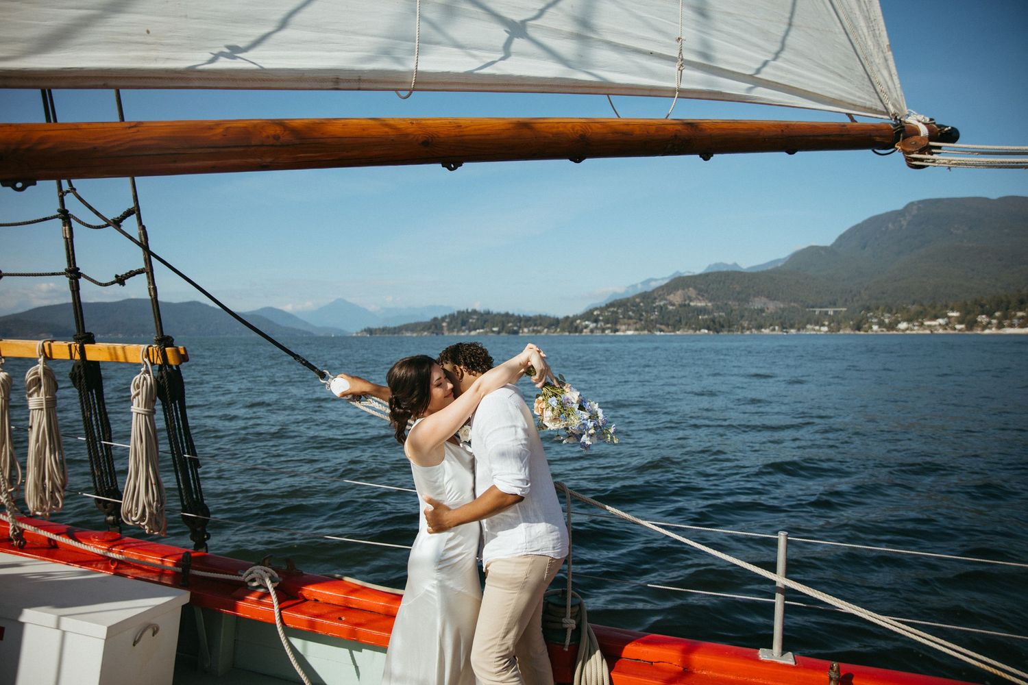Couple kissing and celebrating with champagne on a classic sailboat on a stunning mountain lake.