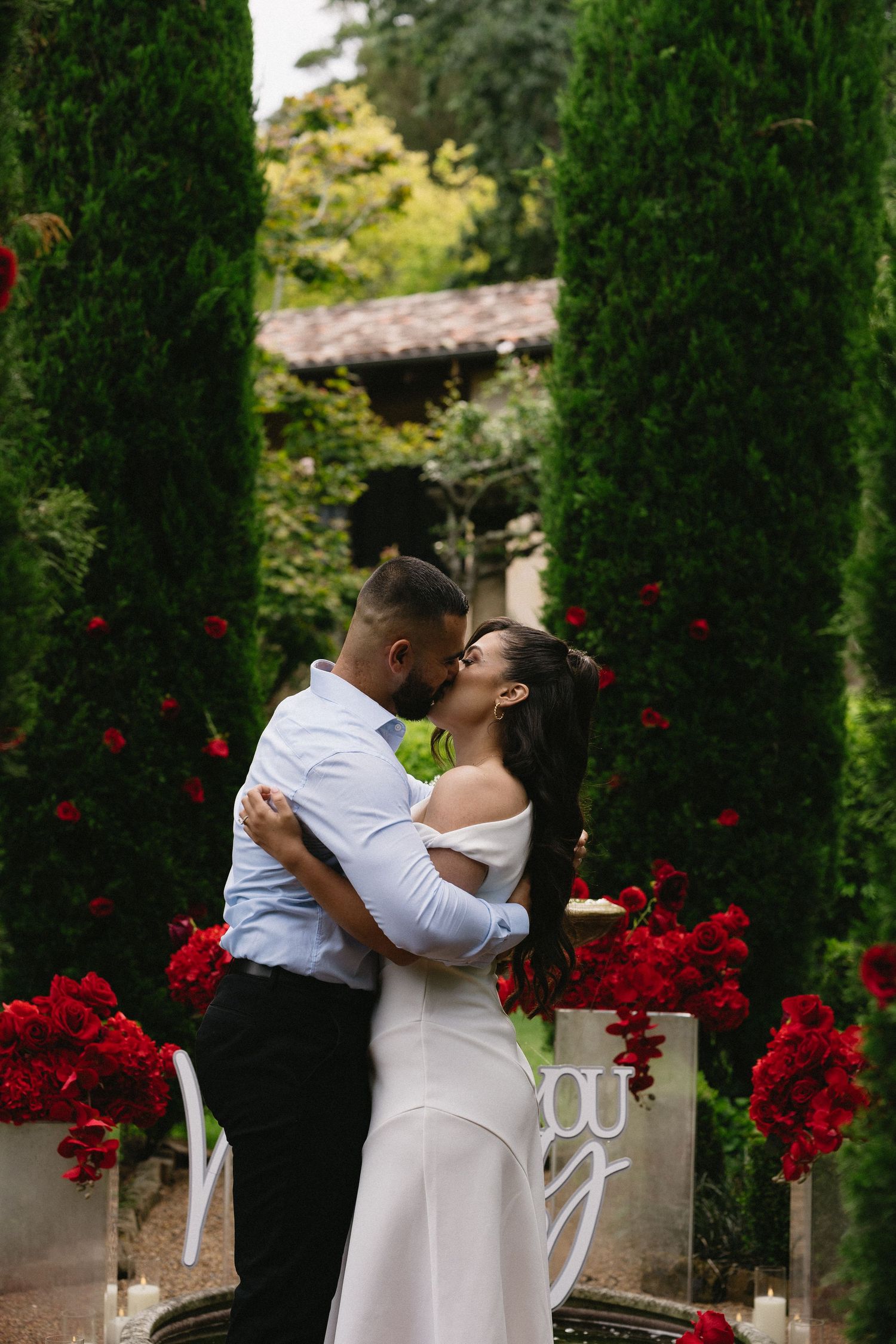 Couple sharing romantic embrace among red roses and garden archway.