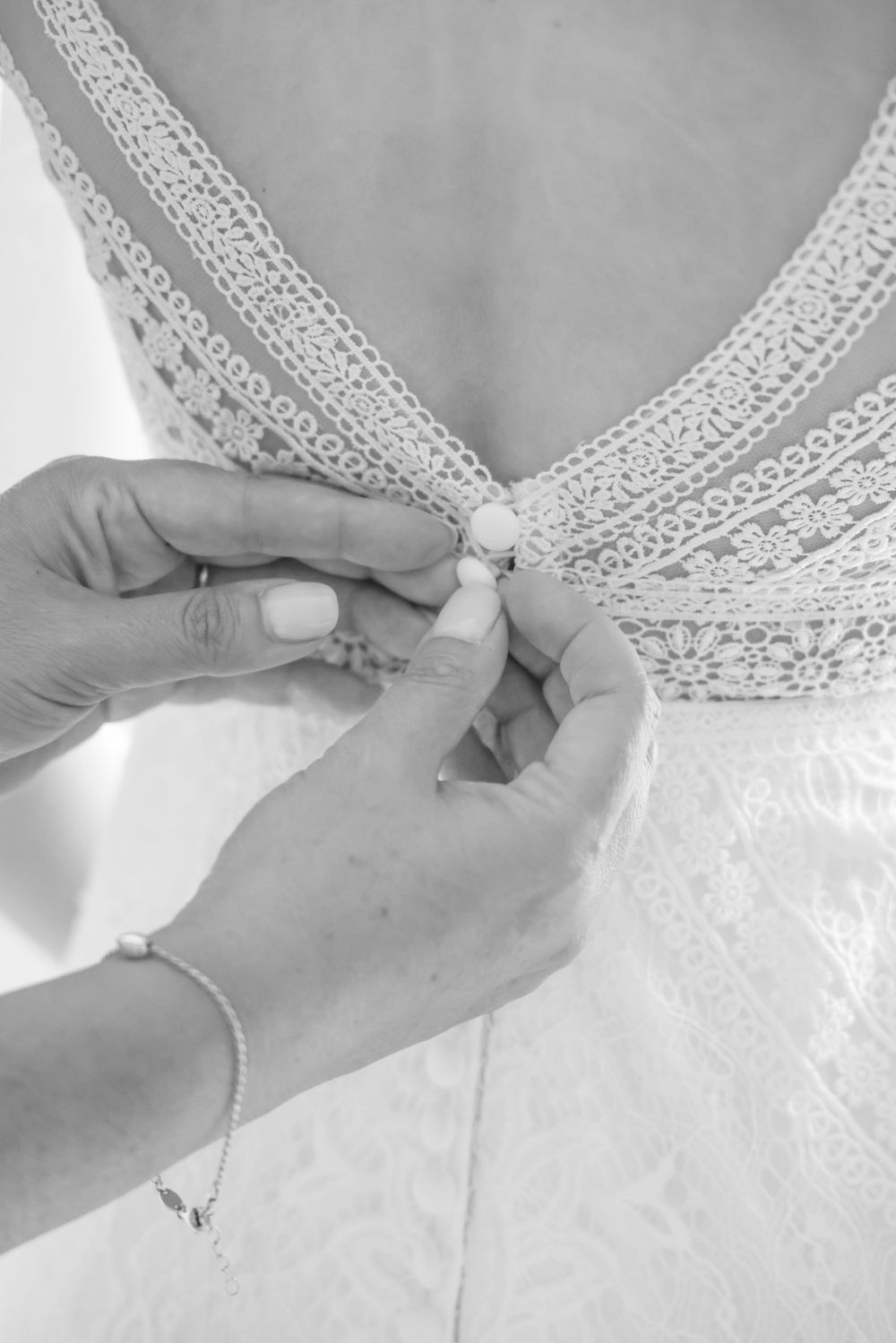 Close-up of hands fastening delicate lace detail on a white wedding dress in black and white