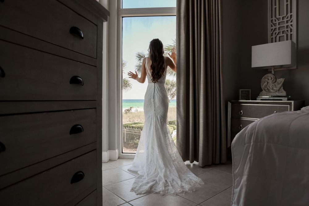 Silhouette of a bride in a fitted lace wedding gown looking out a hotel window.