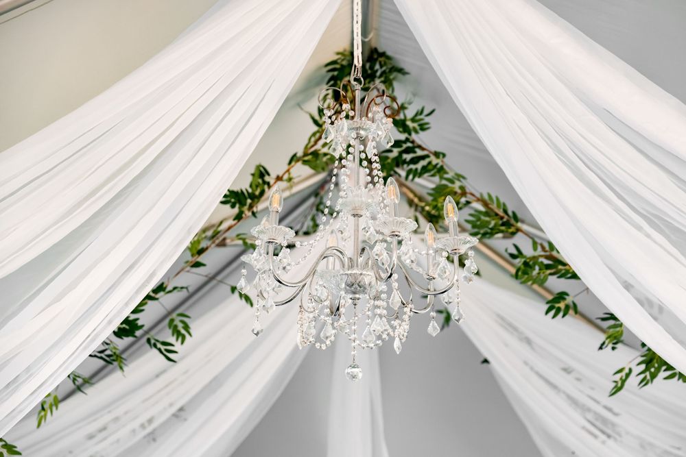 Elegant white draped ceiling with crystal chandelier and green floral accents.