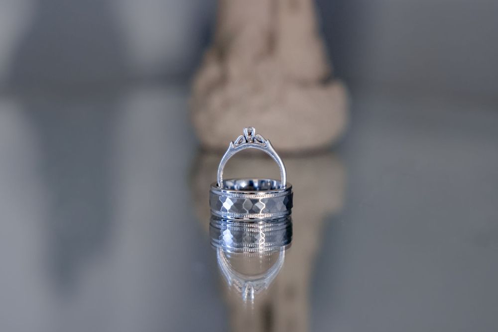 Close up of wedding rings reflecting on a mirrored surface with soft blur effect.
