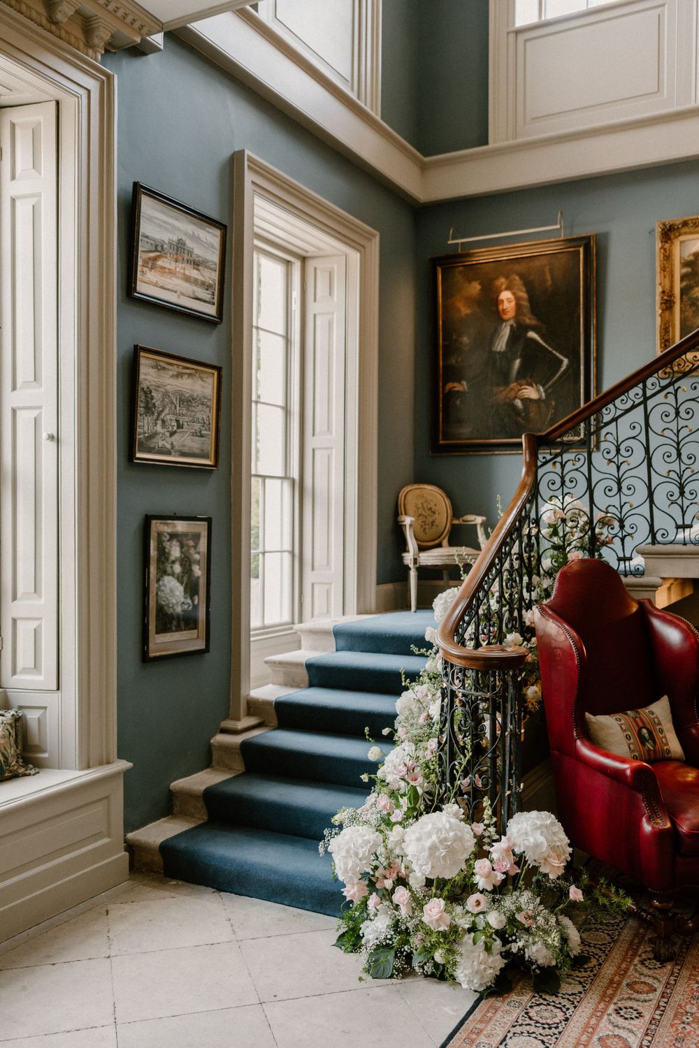 Grand staircase with blue walls, vintage portraits, and white floral decorations.