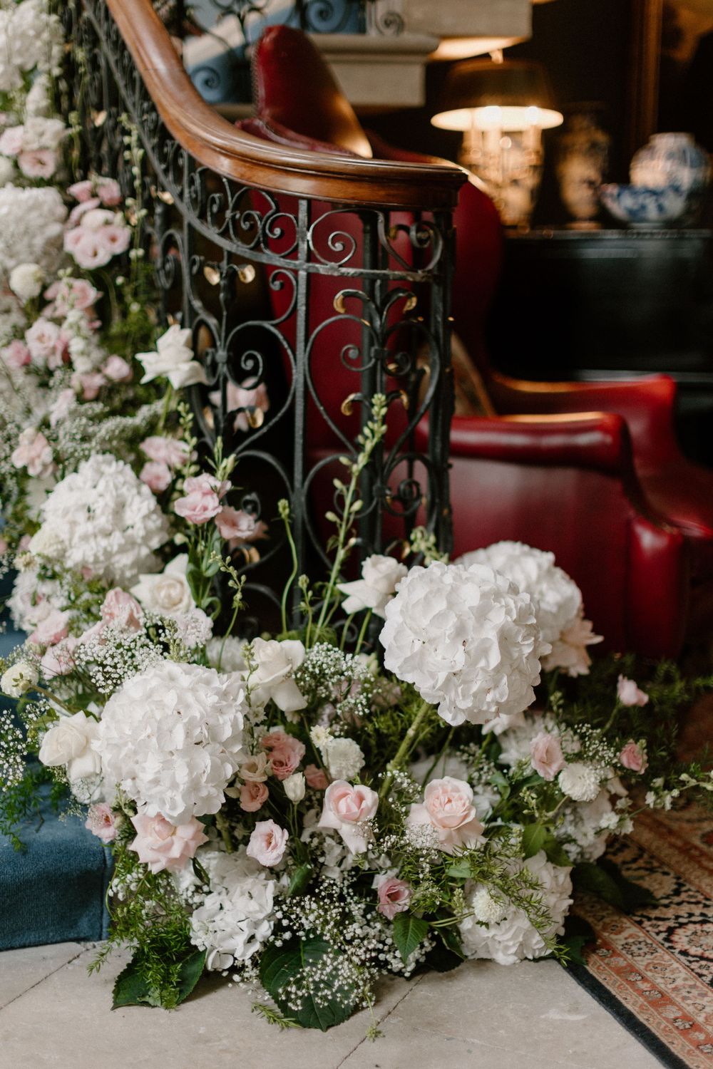 Ornate wrought iron staircase railing with lush white hydrangeas and pink rose arrangements.
