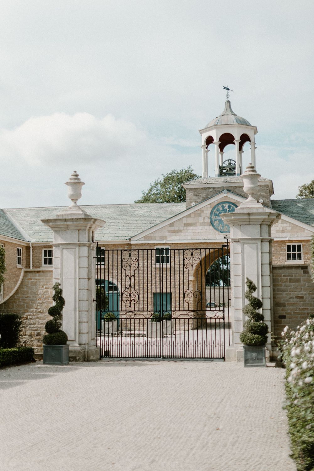 Elegant stone entrance gate with bell tower and topiary decorations.