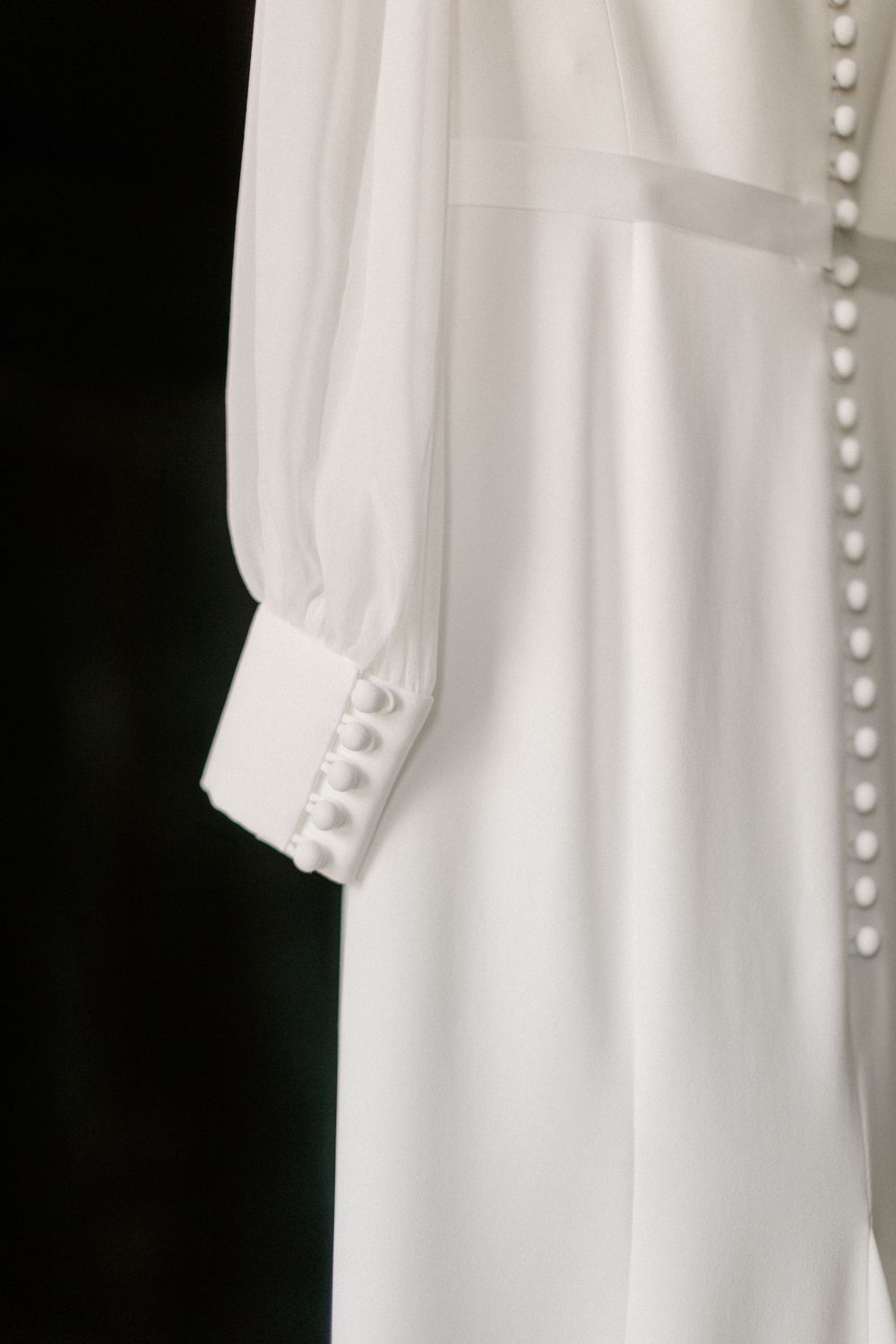 Close-up detail of a white wedding dress sleeve with delicate pearl buttons.