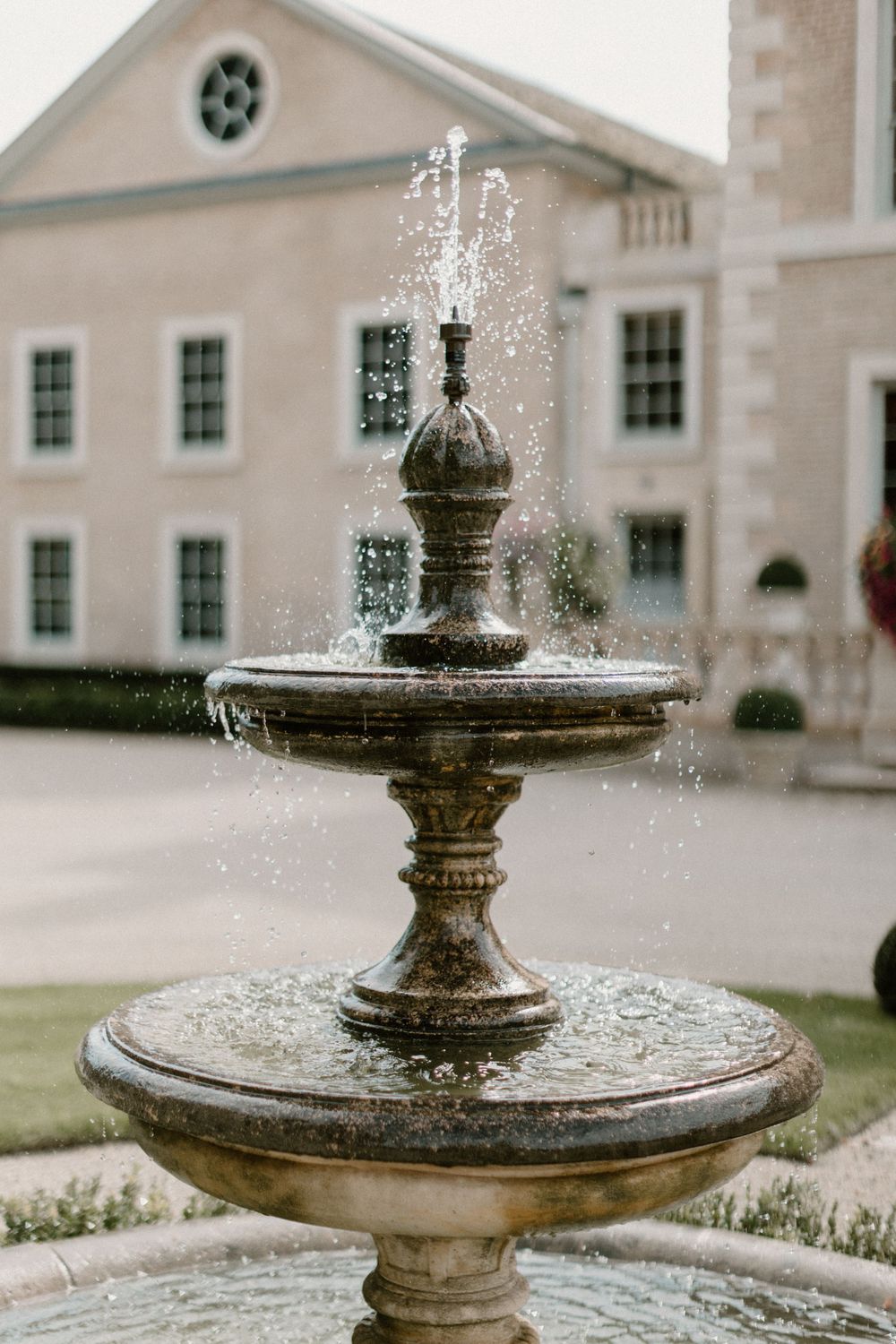 Stone tiered fountain spraying water in front of a classic white building.