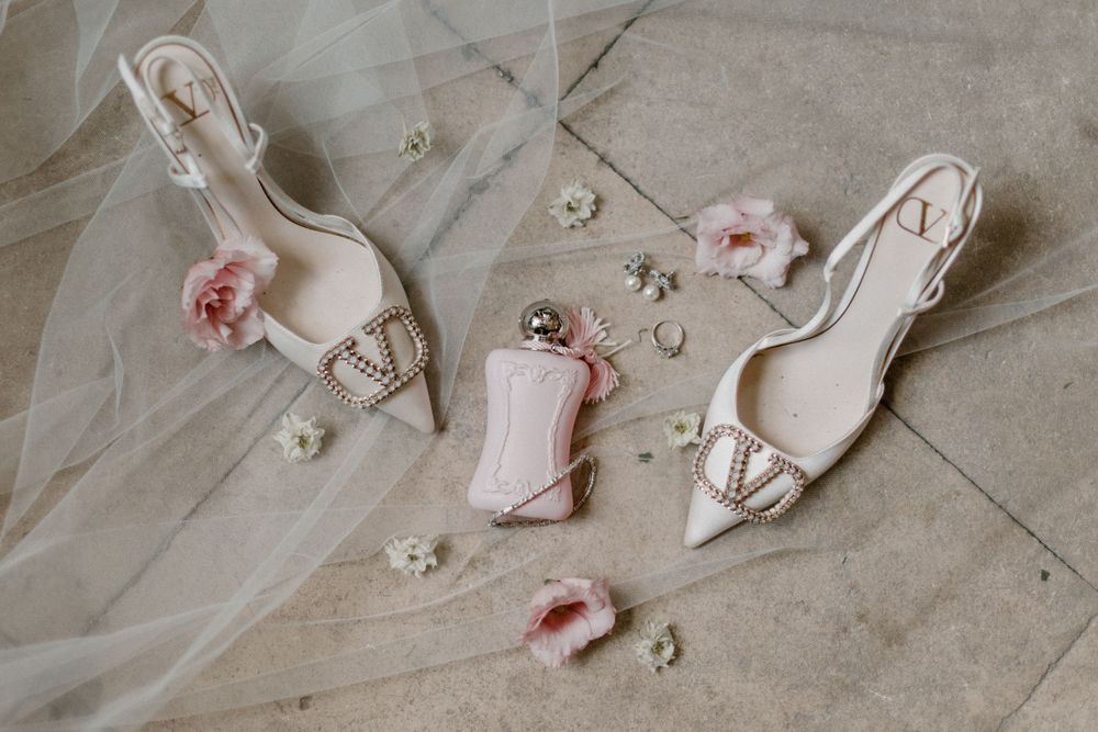 Wedding accessories including white heels and pink perfume bottle on delicate tulle.