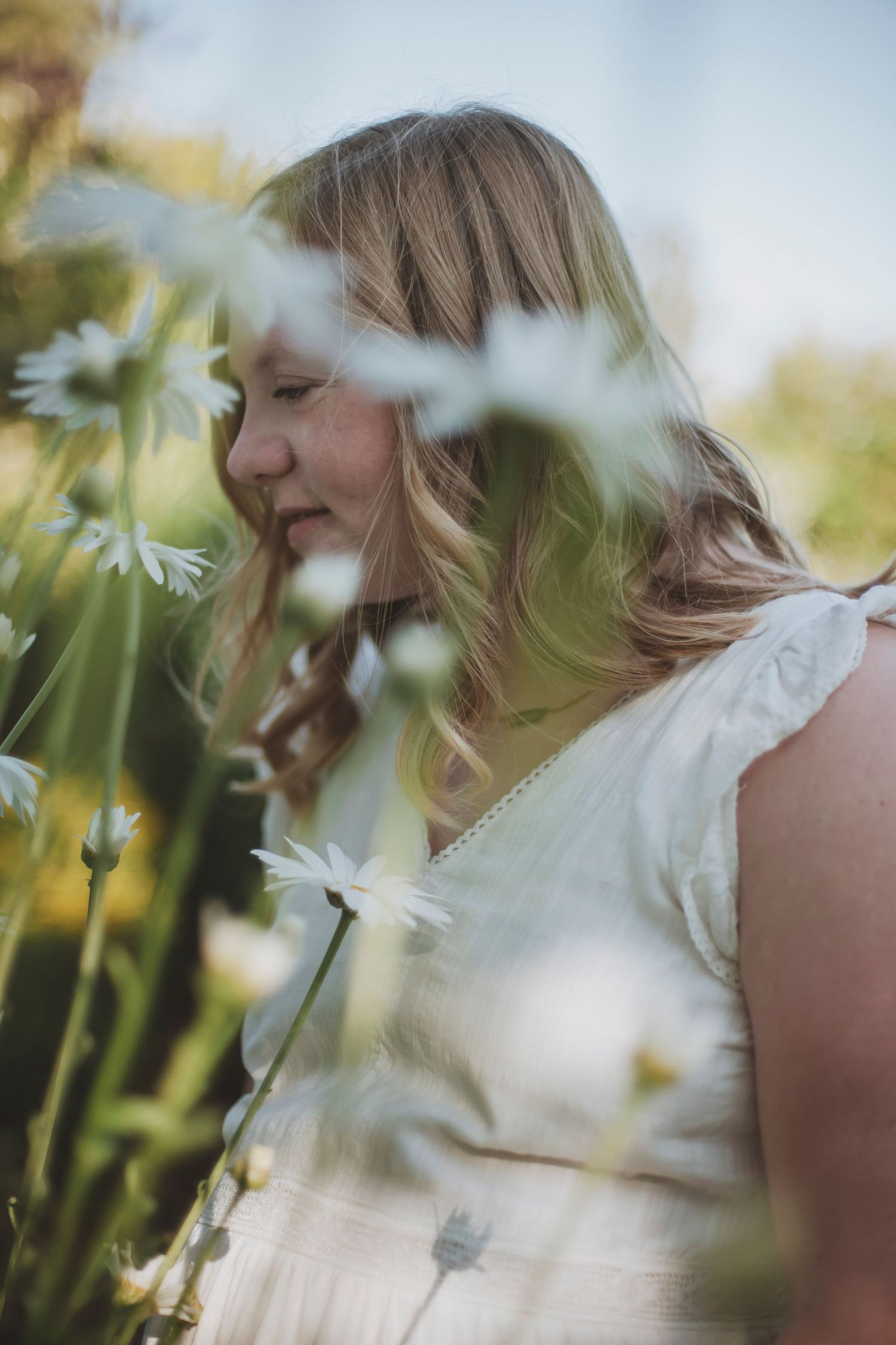 Young girl peacefully enjoying a moment surrounded by tall daisies in a sunlit field.