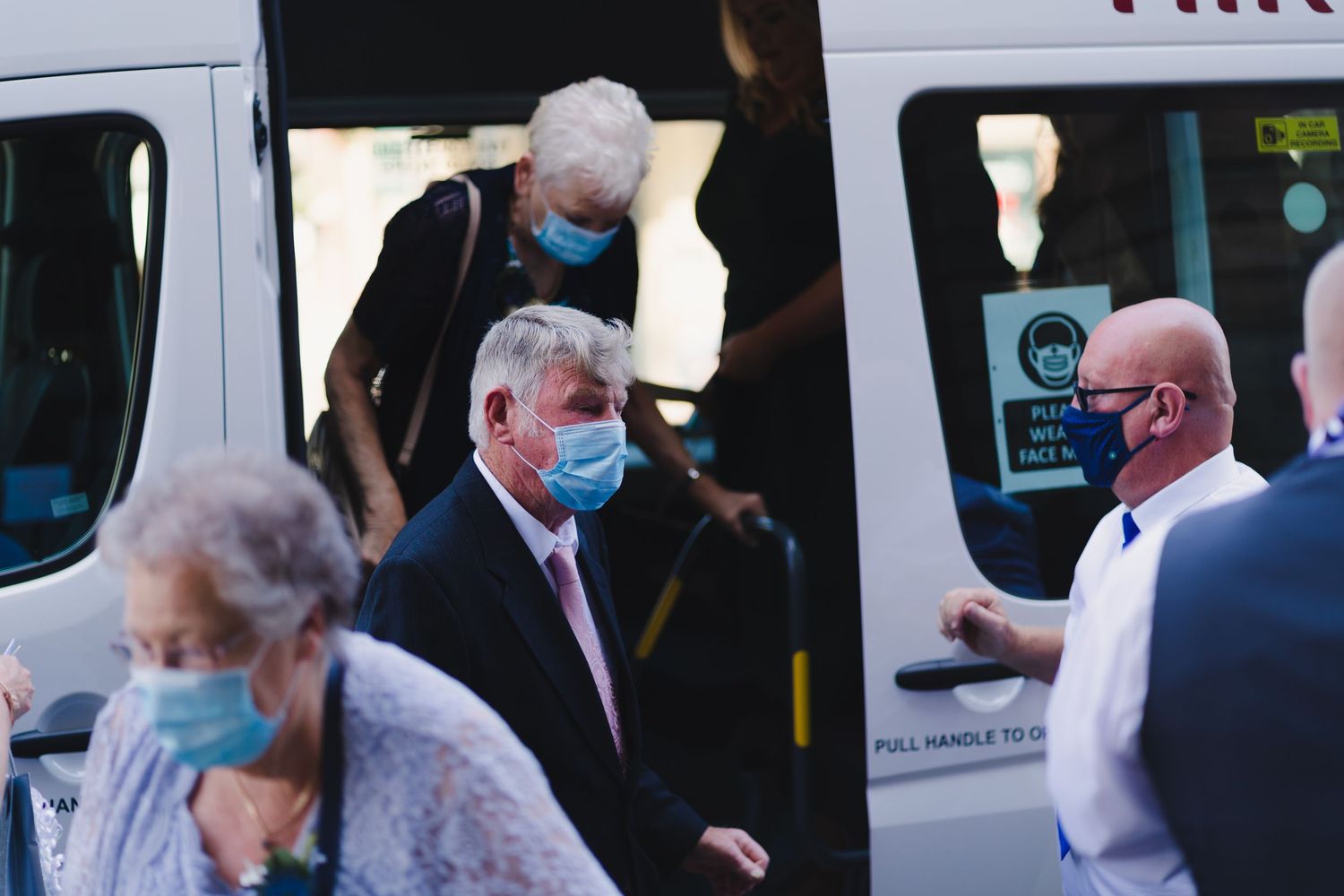 People in masks board a white shuttle van during a group event.