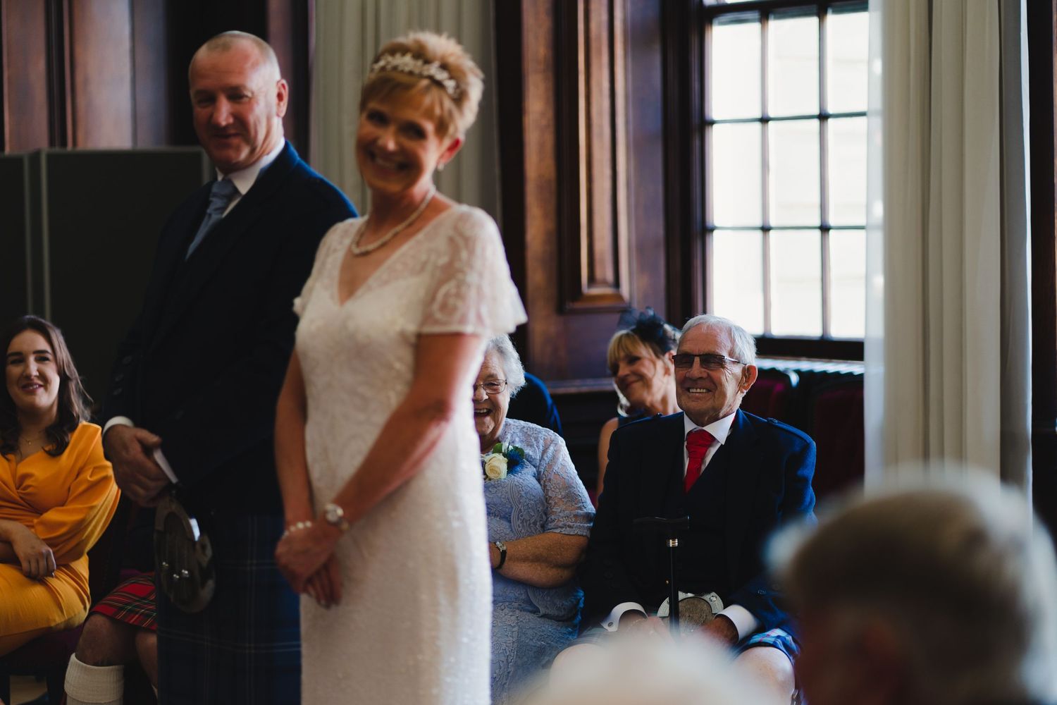 Wedding ceremony in an elegant wood-paneled room with attendees in formal attire.