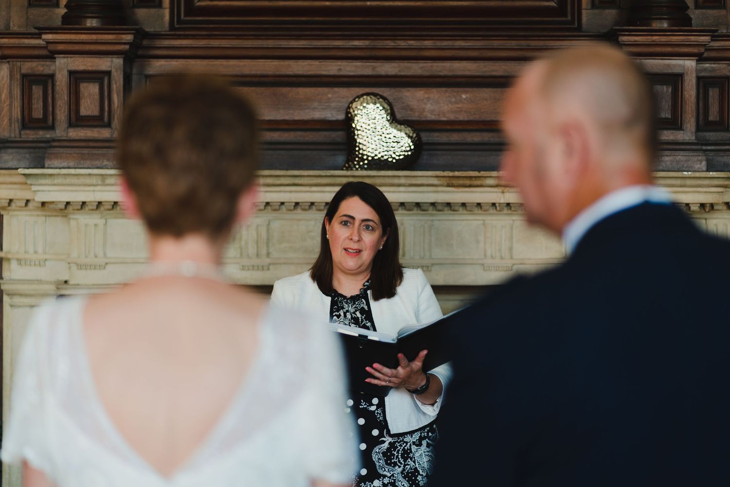 Intimate wedding ceremony with officiant reading from book under decorative heart detail.