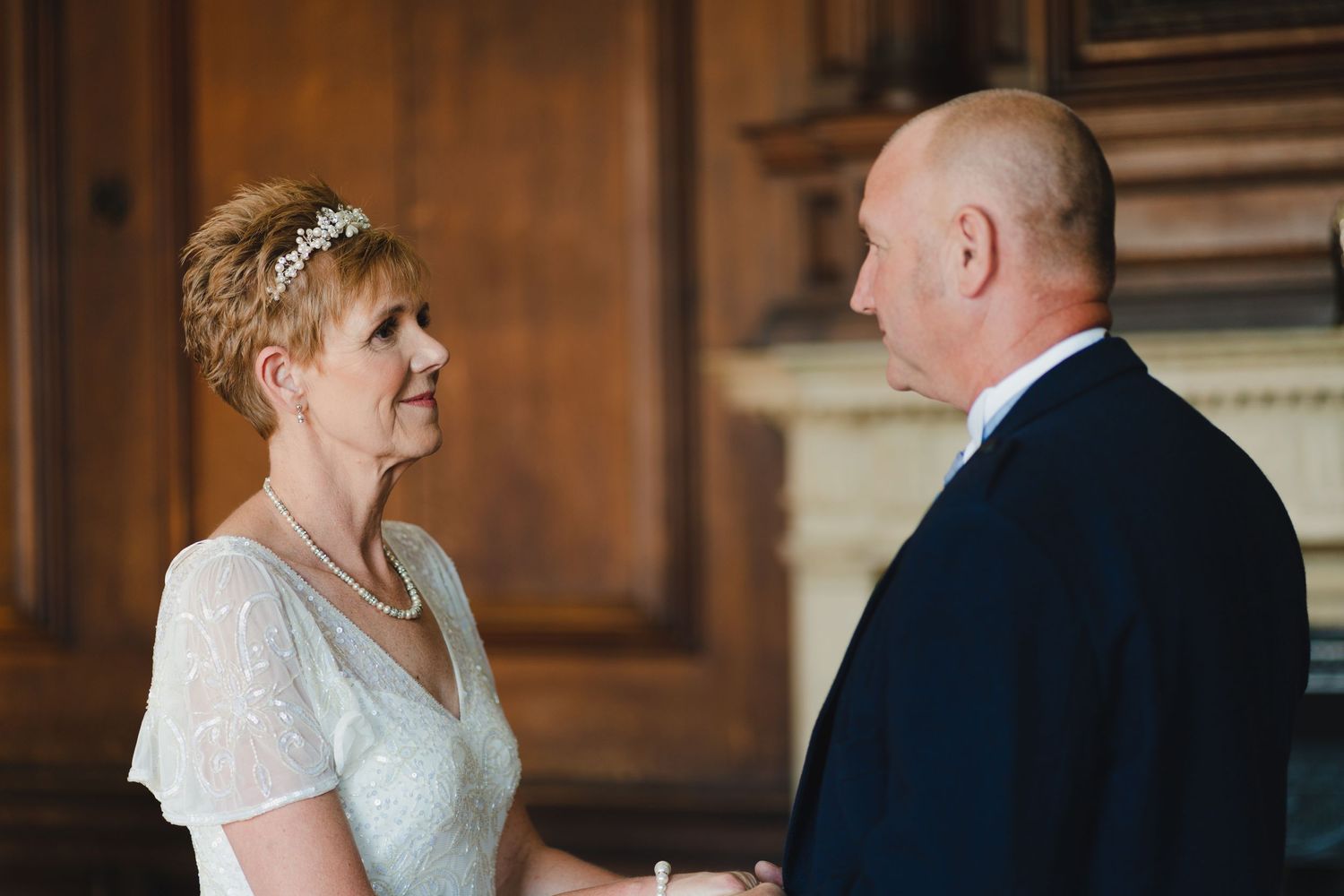 Close up of wedding ceremony exchange in wood-paneled room with warm lighting.