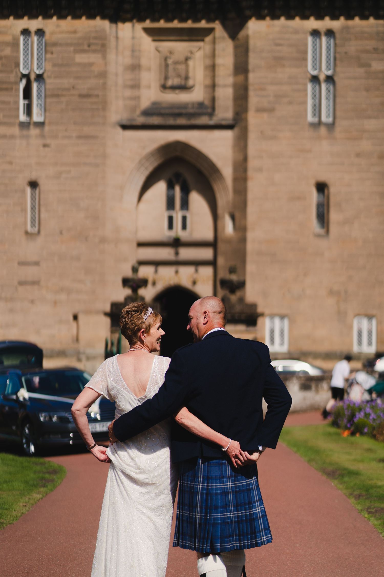 Wedding couple viewed from behind looking at historic castle entrance.