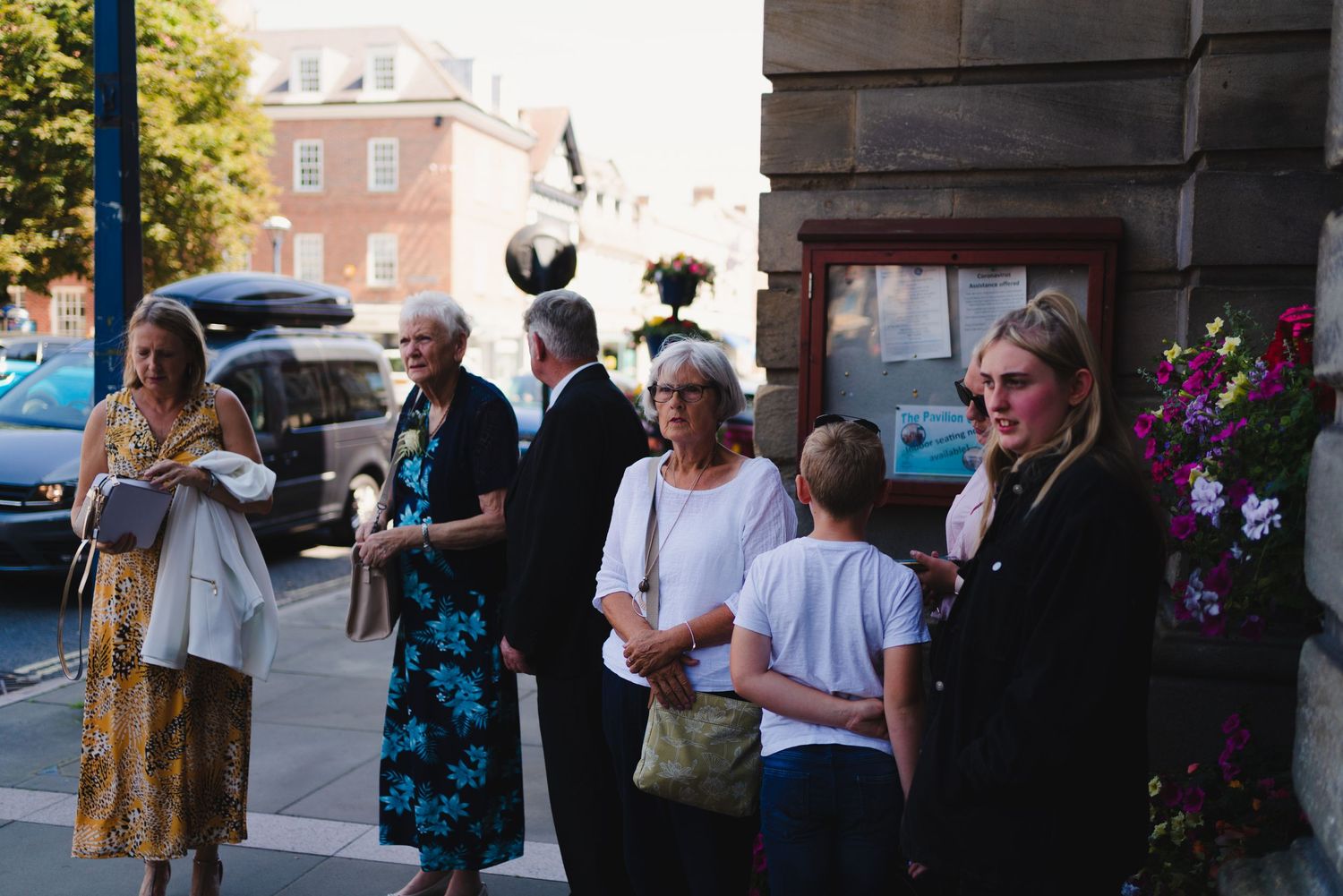 A group of people gathered outside a brick building on a sunny day.