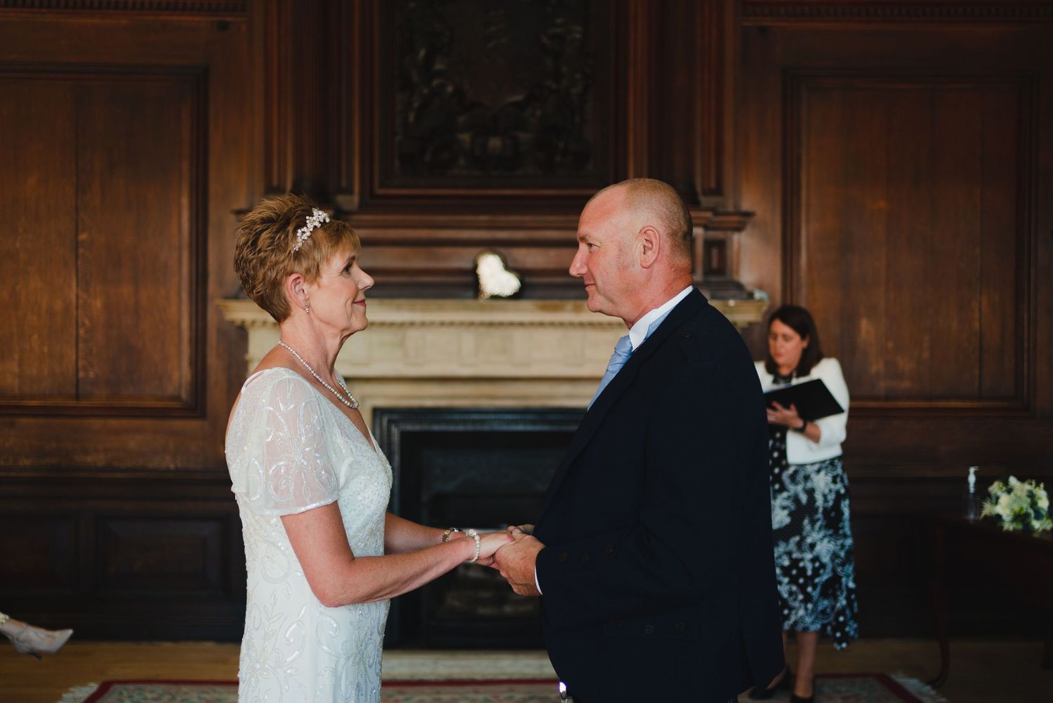 Couple exchanges vows in elegant wood-paneled room during wedding ceremony.