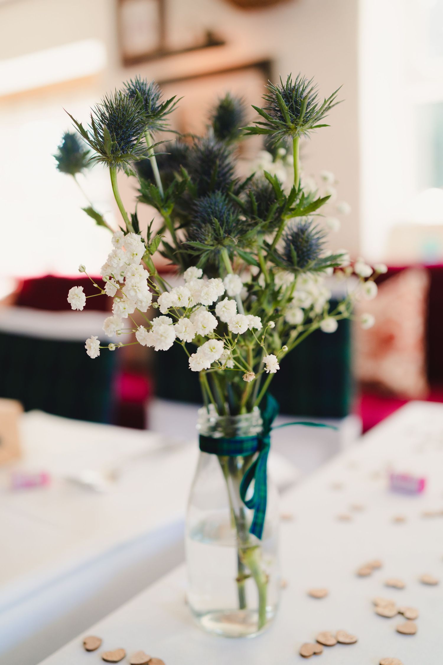 Blue thistle flowers and white blooms arranged in a glass mason jar on a white tablecloth.