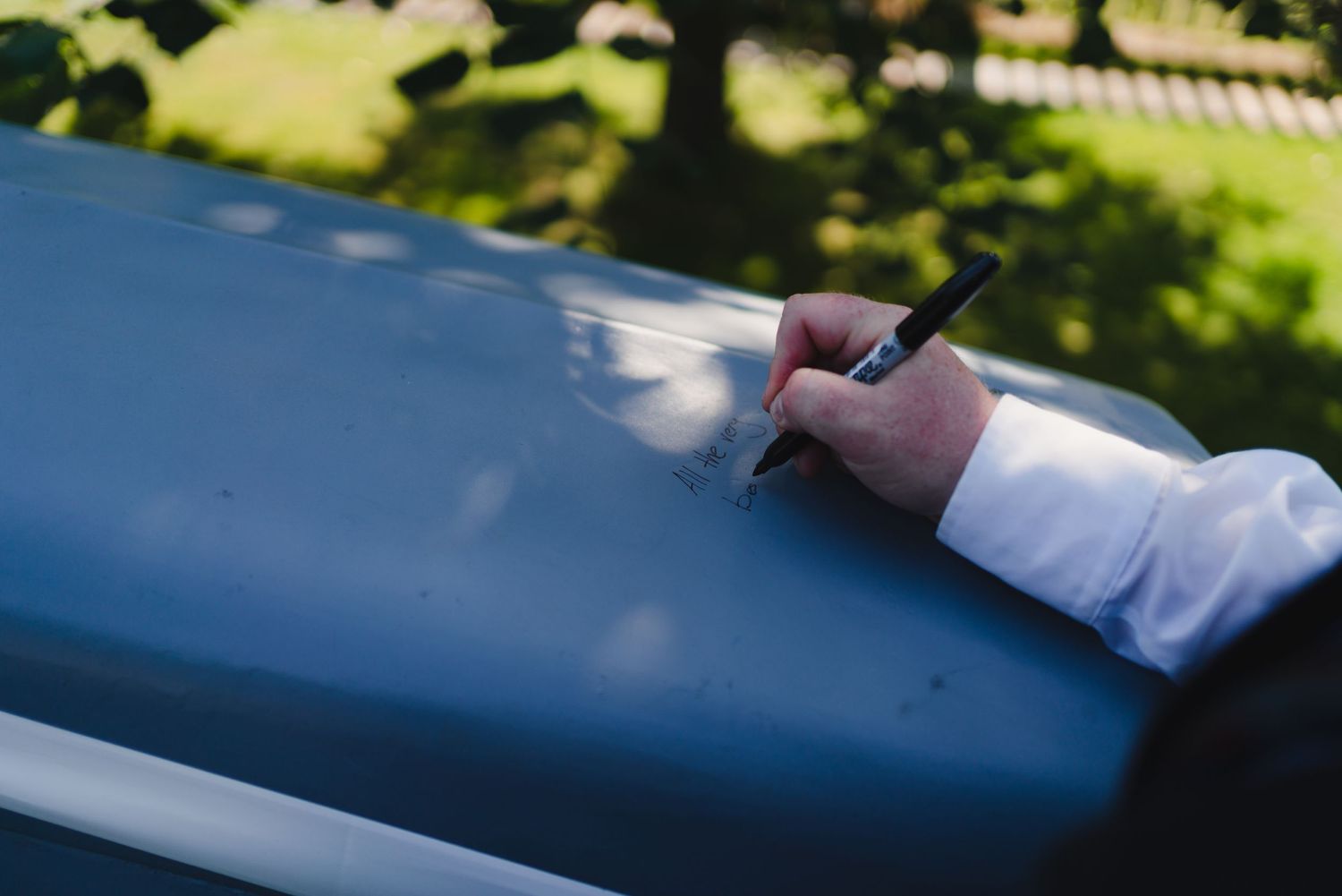 A hand holding a pen against a blue surface in an outdoor setting.