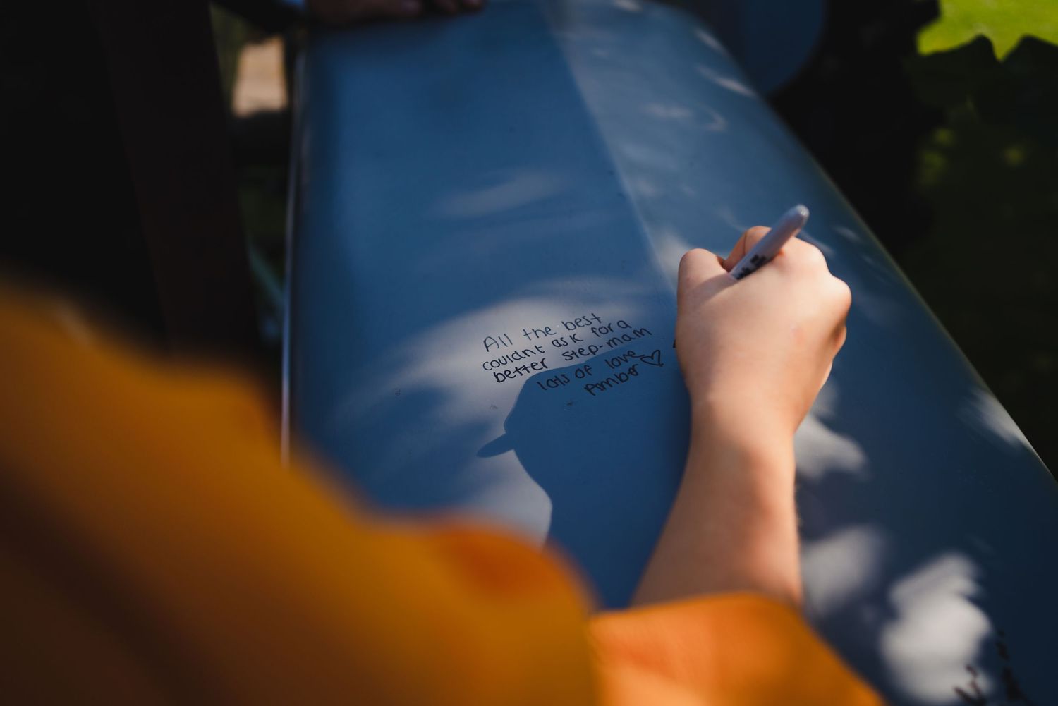 A closeup of someone writing on a blue surface with sunlight creating shadows.