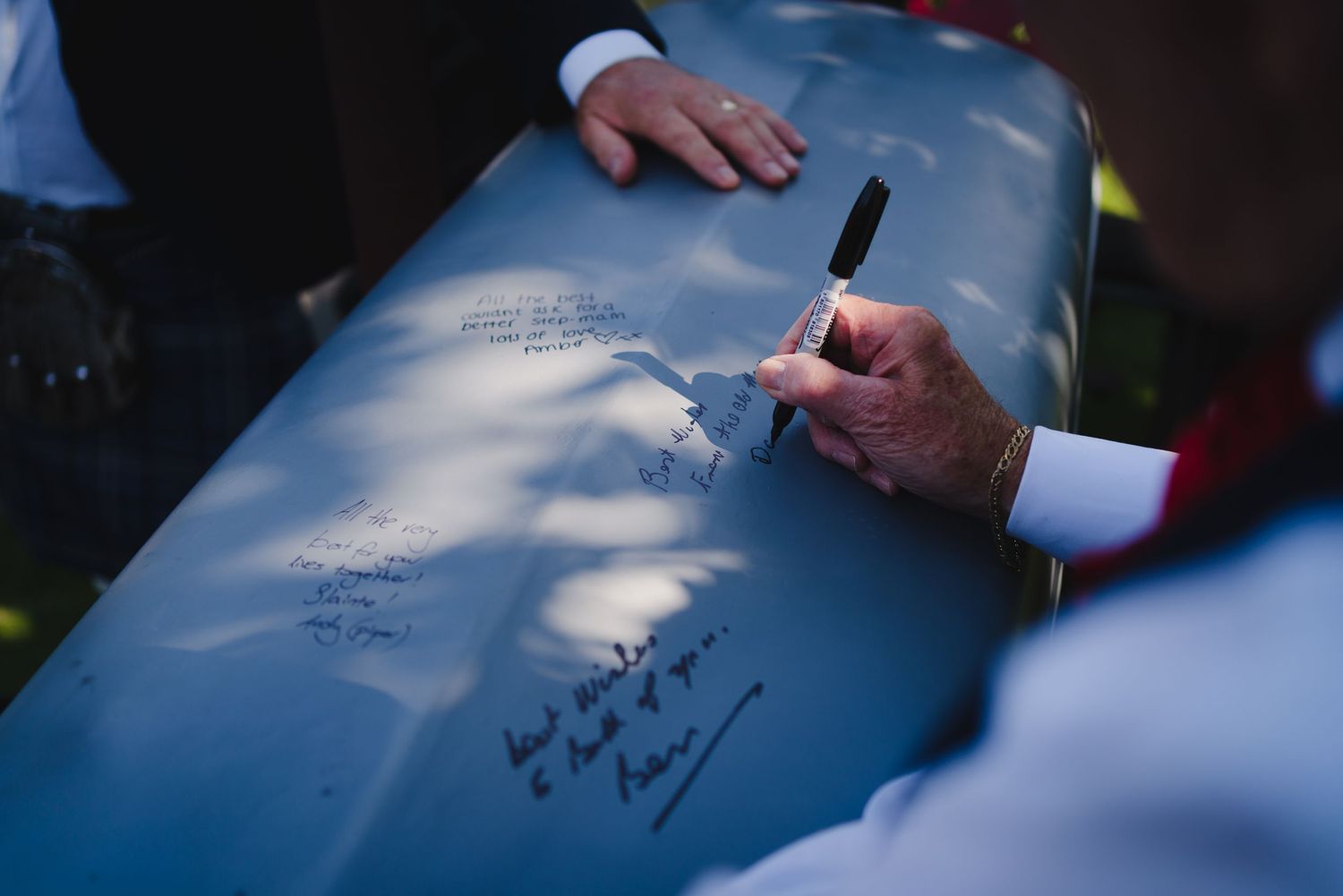 Multiple hands shown signing a blue surface at an outdoor event.